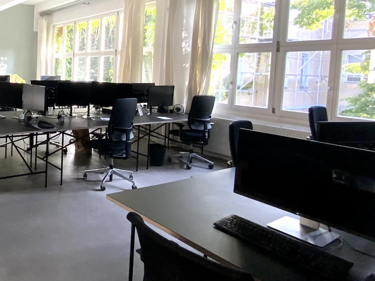 Open-plan office with rows of desks, monitors, and tall windows