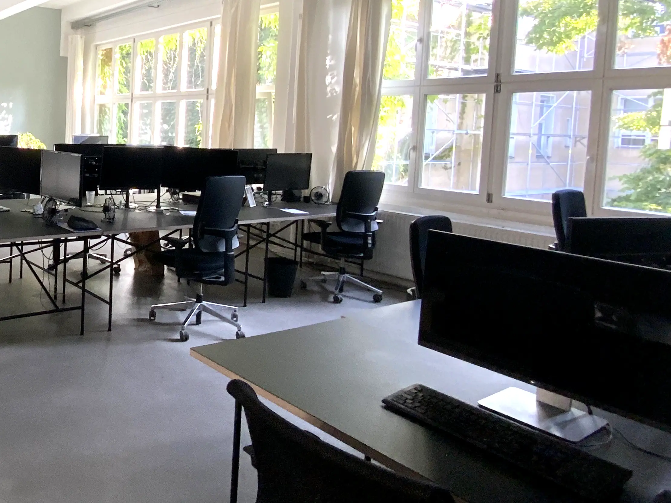 Open-plan office with rows of desks, monitors, and tall windows